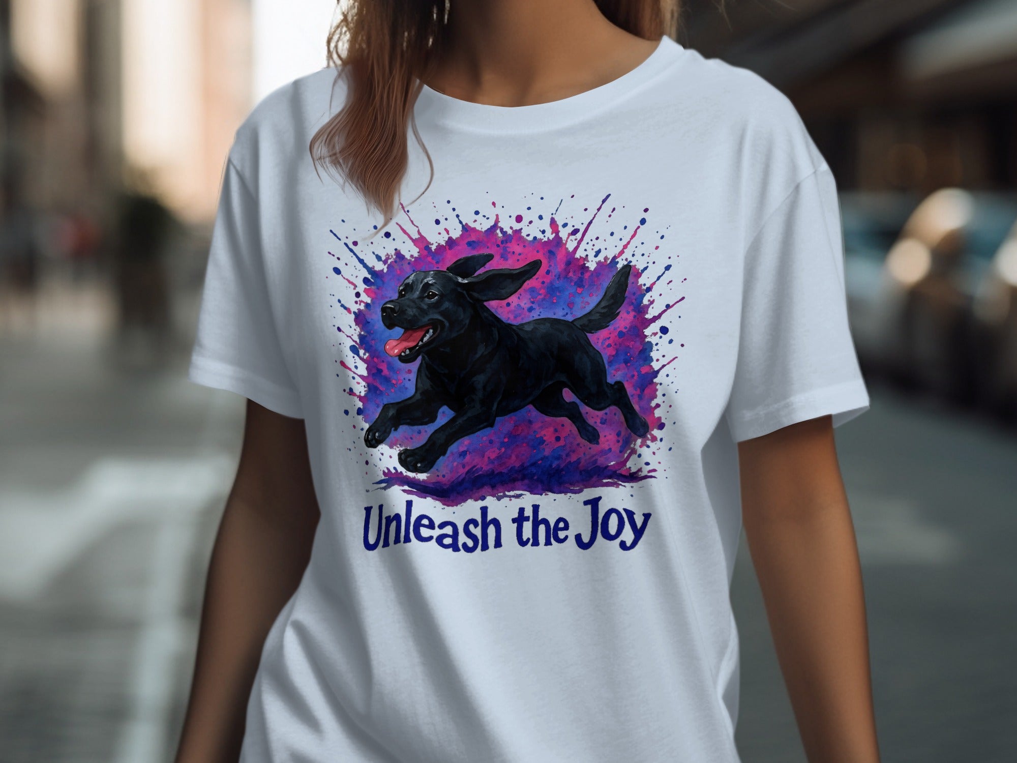 White t-shirt with a black dog running through purple and pink paint splatters, text "Unleash the Joy".