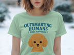 Light green t-shirt with cartoon poodle and "Outsmarting Humans Since Puppyhood" text.