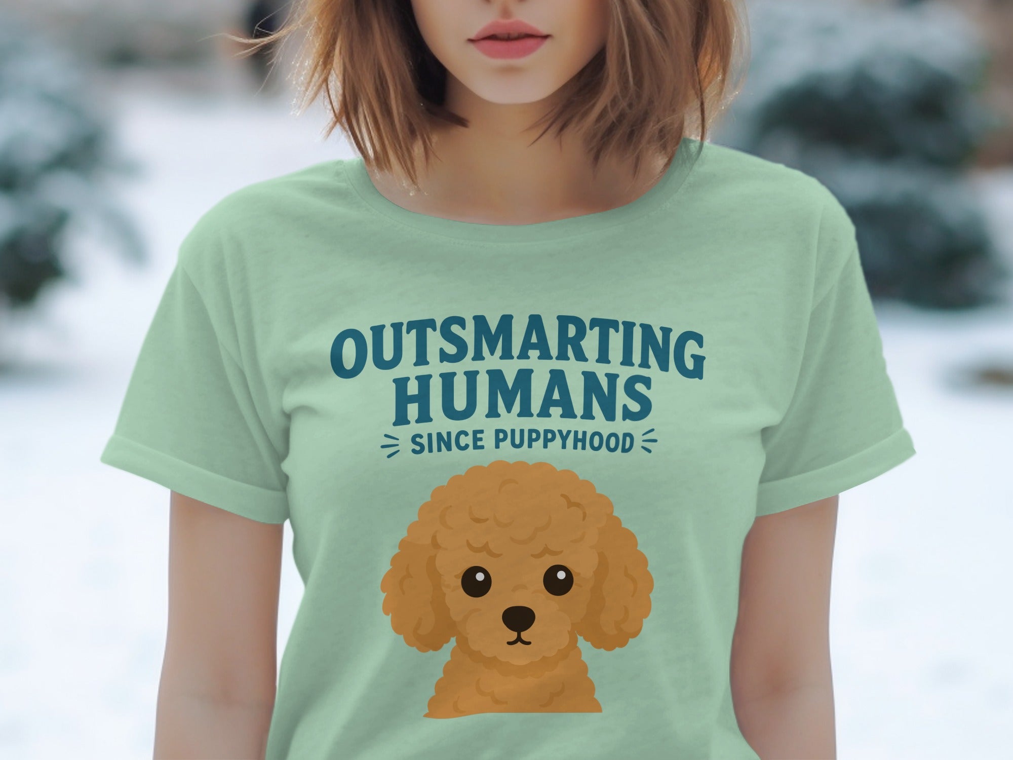 Light green t-shirt with cartoon poodle and "Outsmarting Humans Since Puppyhood" text.