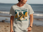 Man in t-shirt with dog graphic and "Always Operating At Full Capacity" text.