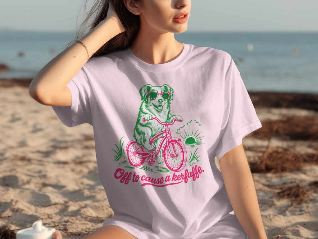 Pink t-shirt with a dog riding a bicycle and the text "Off to cause a kerfuffle."