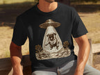 Black t-shirt with a pug being abducted by a UFO in a desert landscape illustration.