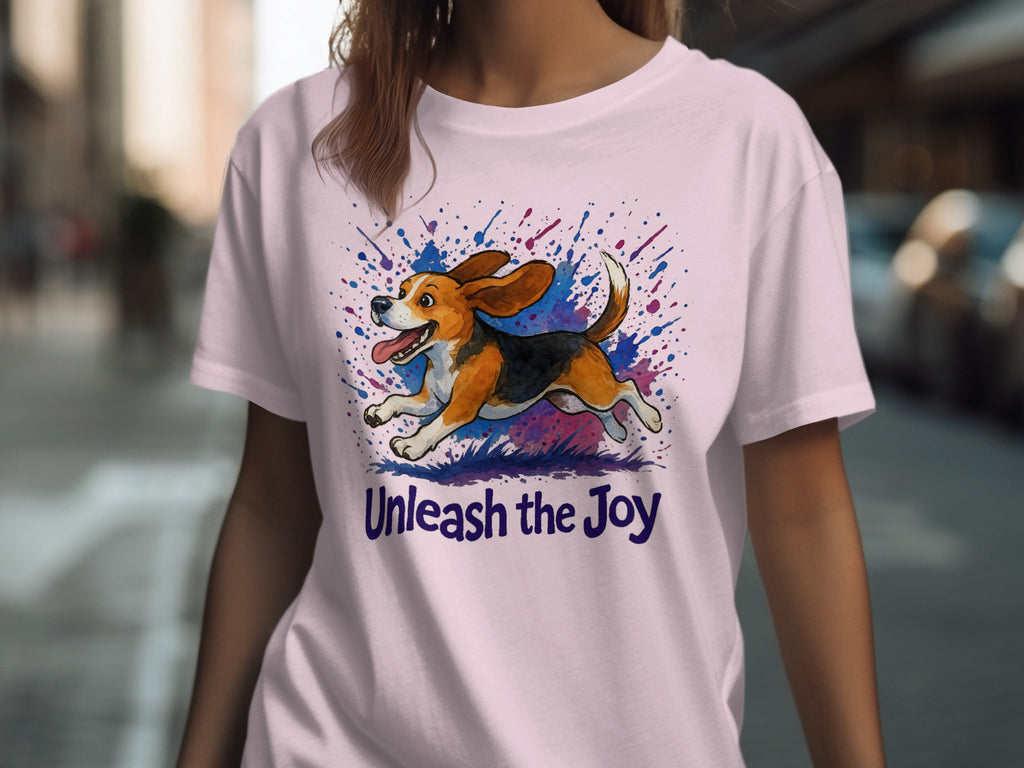 Pink t-shirt featuring a watercolor beagle mid-run with splattered ink and text "Unleash the Joy."