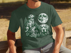 Green t-shirt with white drawing of three dogs, trees, and a full moon.
