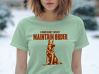 Light green t-shirt with a seated dog and "SOMEBODY MUST MAINTAIN ORDER" text.