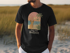 Black t-shirt with a French bulldog on a beach at sunset, "Paws And Reflect" text.