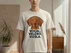 Vizsla dog head graphic with "VOCAL. VELCRO. VIZSLA." text on a cream t-shirt.