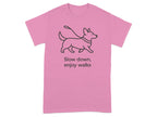 Pink t-shirt with a black line drawing of a dog on a leash and text "Slow down, enjoy walks".