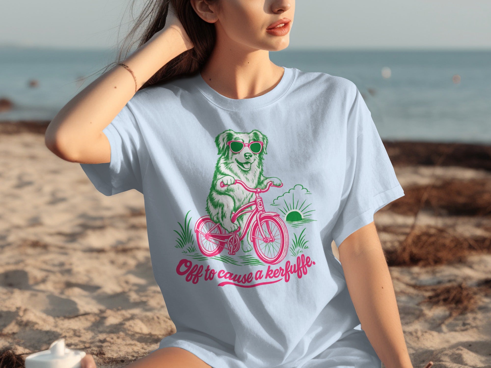 Dog in sunglasses riding a pink bicycle on a beach, text "Off to cause a kerfuffle".