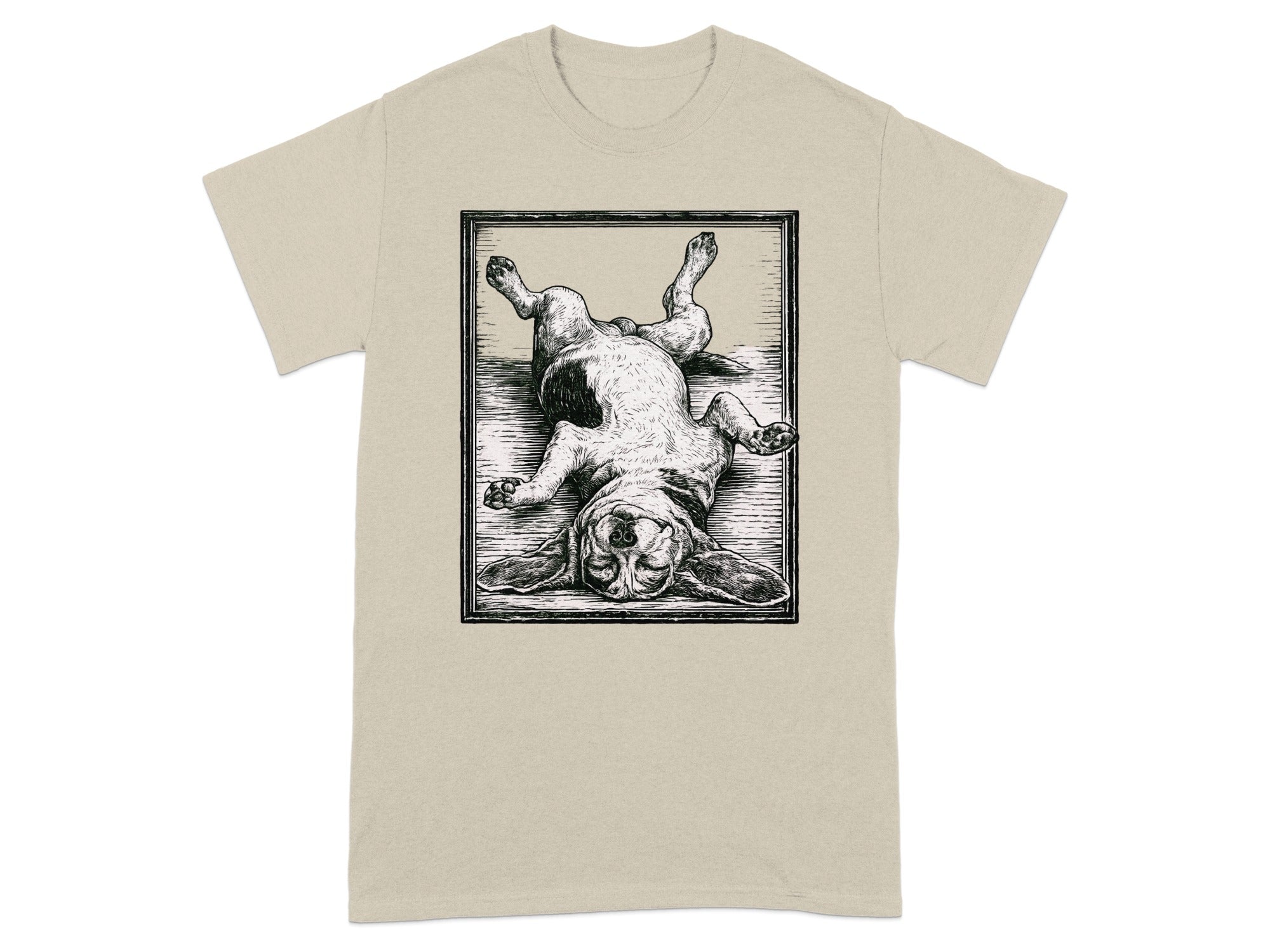 Black and white illustration of a dog lying on its back inside a framed rectangle on a tan t-shirt.