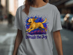 Light gray t-shirt with a yellow dog mid-leap over purple and blue paint splashes, text below says "Unleash the Joy".