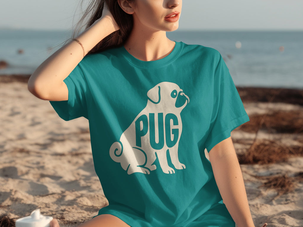 Teal t-shirt with white pug art and the word "PUG" on a beach.