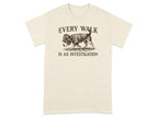 T-shirt with beige fabric, featuring a dog in a hat and coat, text reads "EVERY WALK IS AN INVESTIGATION".