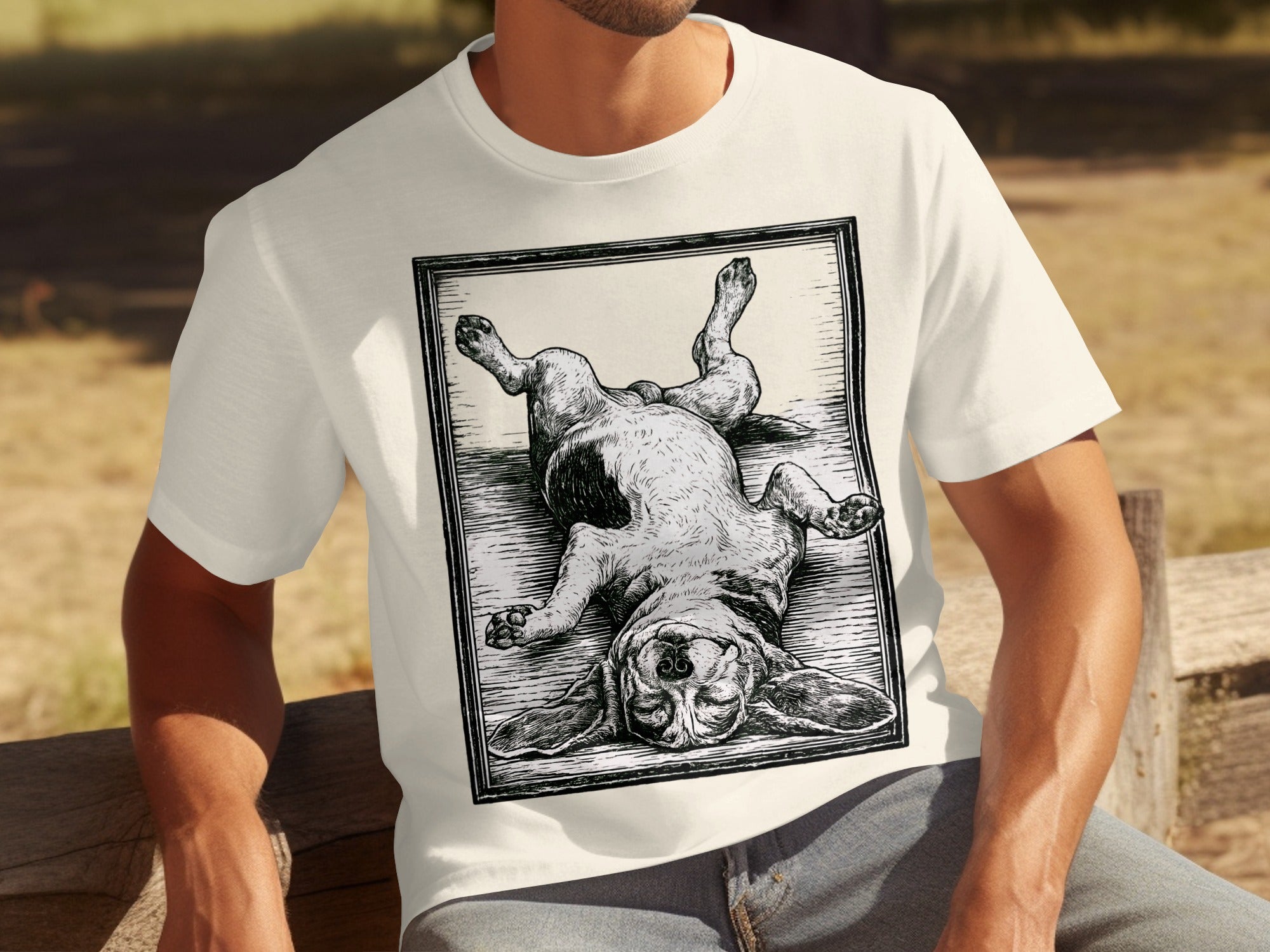 Cream t-shirt with a black and white woodcut-style print of a basset hound lying on its back.