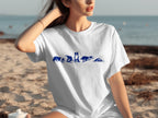 White t-shirt with blue dog silhouettes in various poses on a beach background.