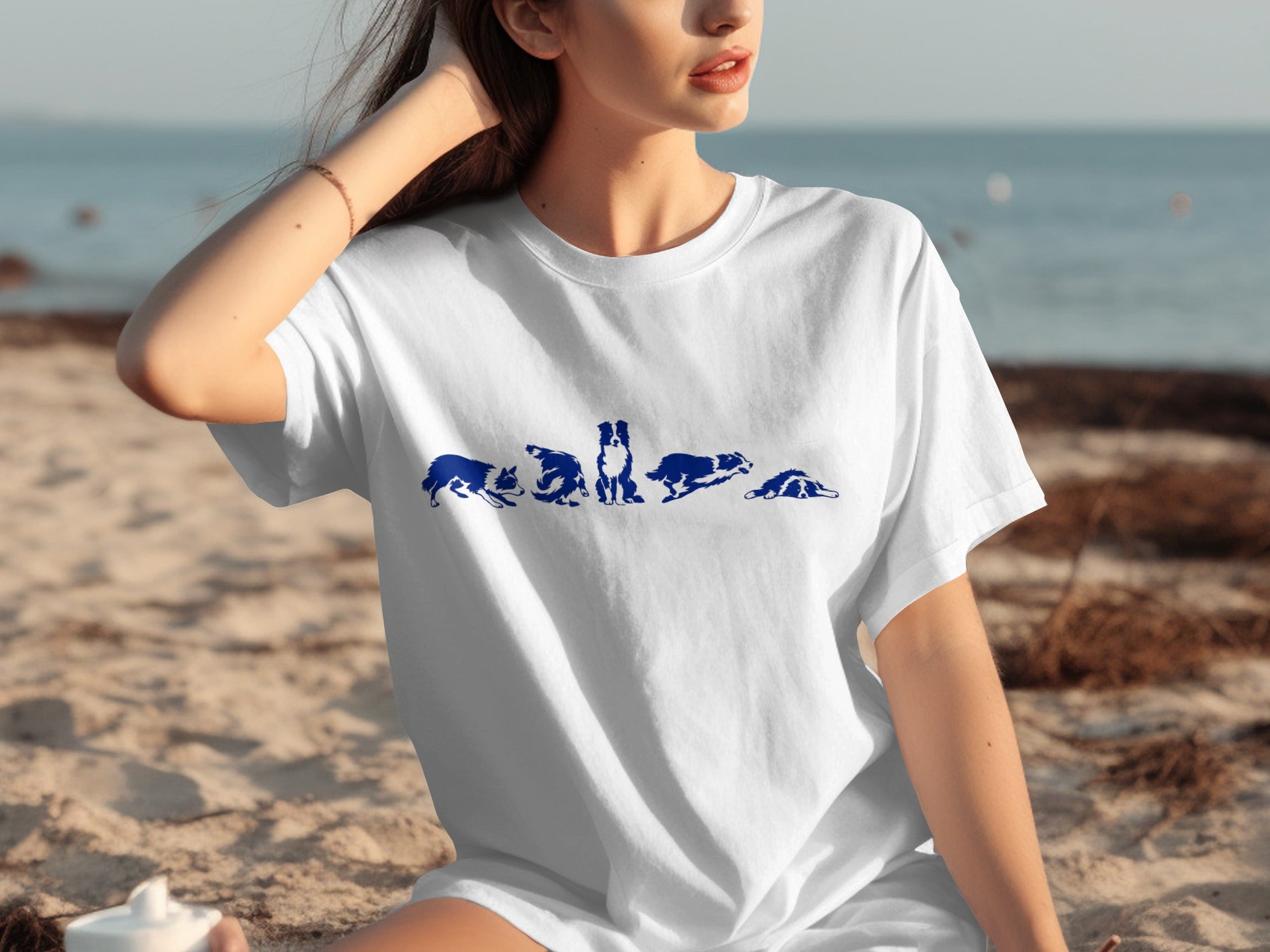 White t-shirt with blue dog silhouettes in various poses on a beach background.