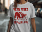 White t-shirt with red text "HERD FIRST. EXPLAIN LATER." and a red border collie.