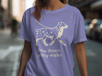 Purple t-shirt with a cream line drawing of a dog and text: "Slow down, enjoy walks."