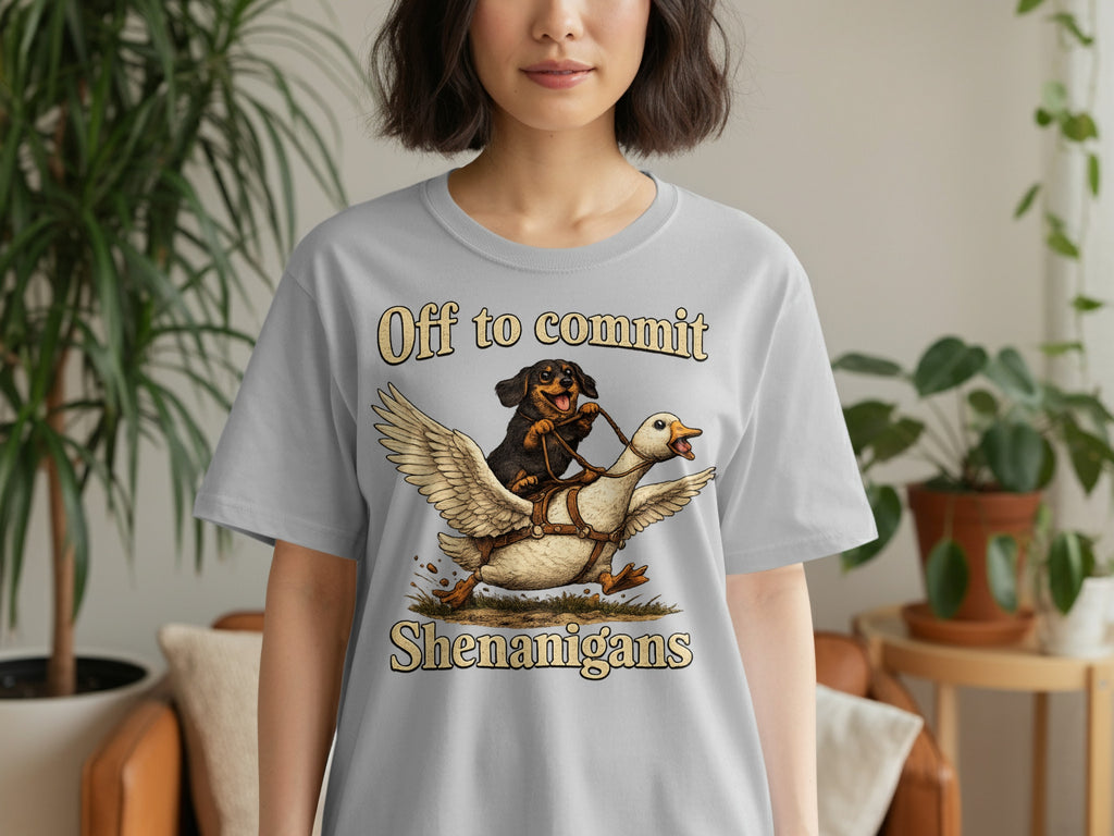 Grey t-shirt with illustration of a dog riding a duck, text "Off to commit Shenanigans".