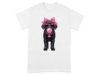 Black Labrador puppy with pink bow, sunglasses, and heart-shaped tag with "GIRL"