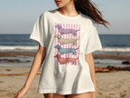 White t-shirt with four colorful dachshunds stacked on a pink striped background.
