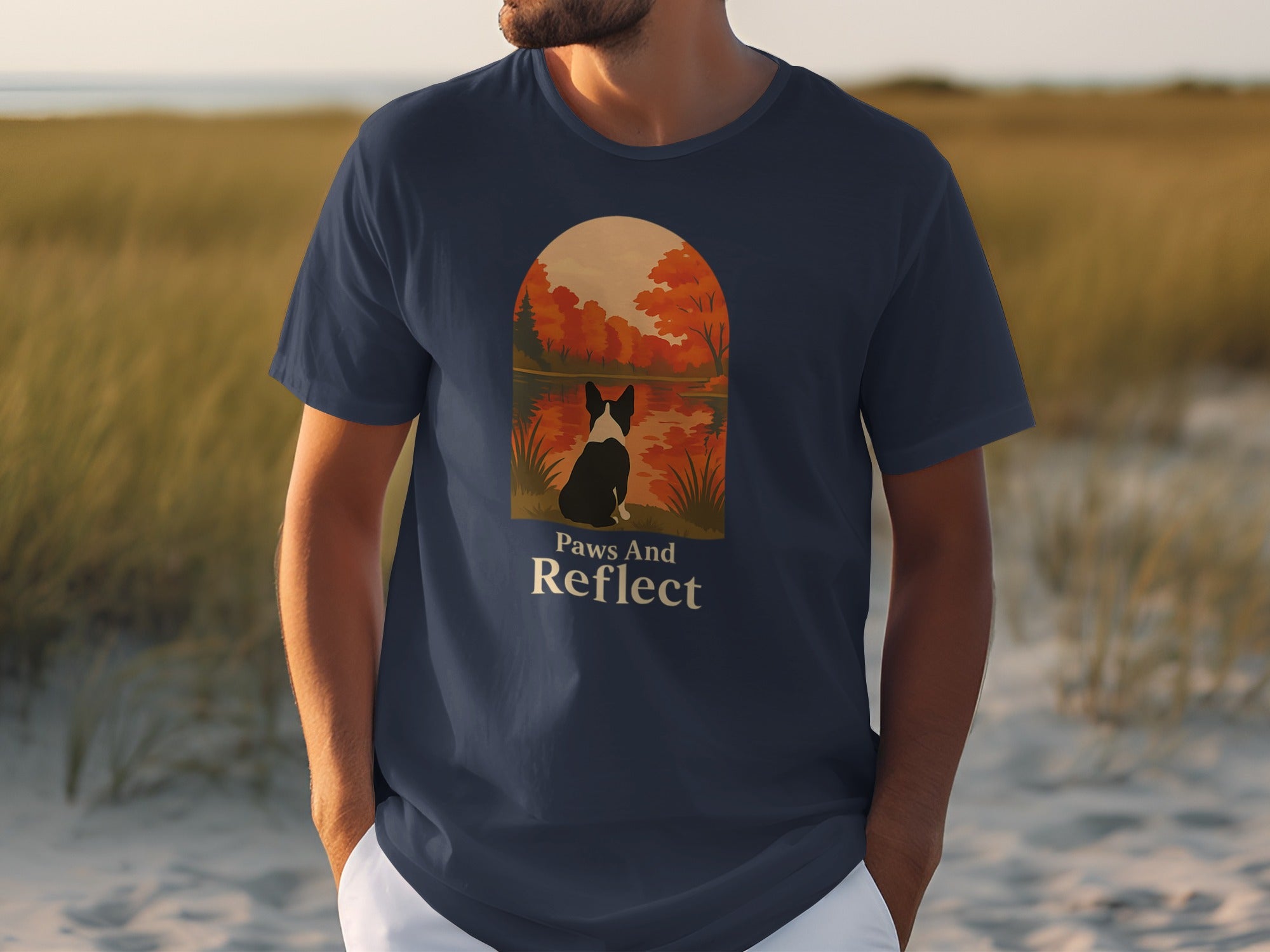 Dark blue t-shirt with graphic of dog, "Paws And Reflect" text, against autumn sunset.