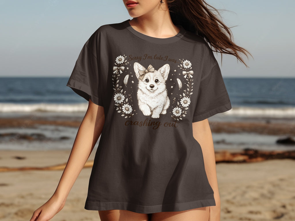Dark t-shirt graphic of a corgi with a bow, framed by flowers. Text reads "Sorry I'm late I was crashing out".