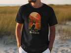 Black t-shirt with dog sitting by autumn lake graphic and "Paws And Reflect" text.