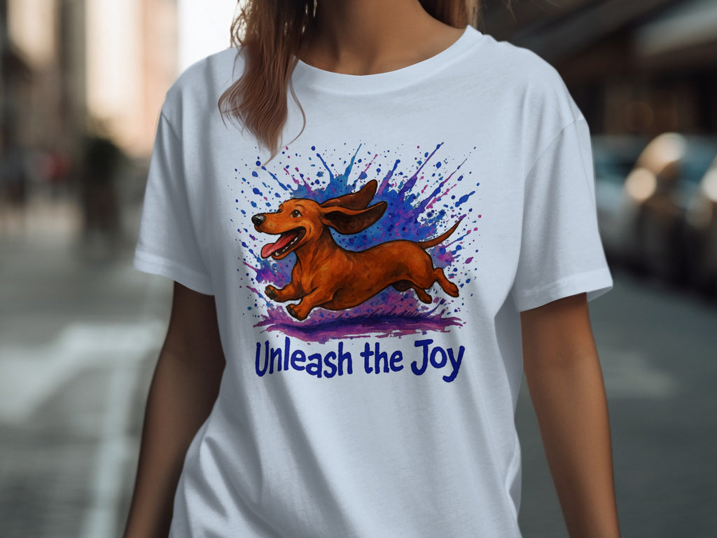 White t-shirt with brown dachshund jumping with colorful paint splatters and text "Unleash the Joy".