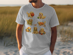 White t-shirt with seven illustrations of golden retriever puppies interacting with yarn.