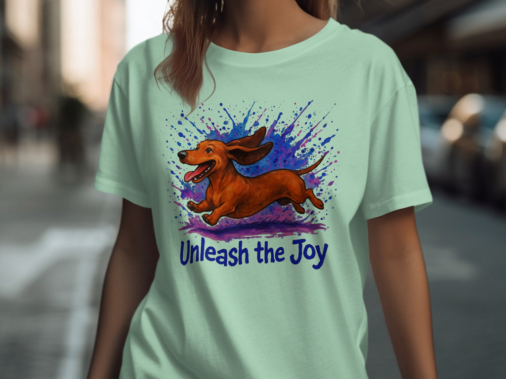 Light green t-shirt with running dachshund illustration and "Unleash the Joy" text.