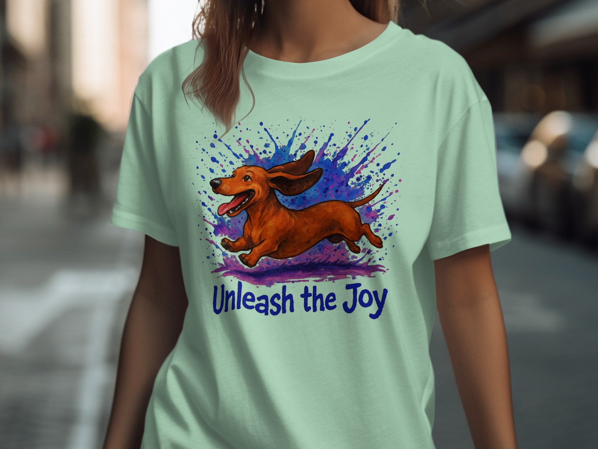 Light green t-shirt with running dachshund illustration and "Unleash the Joy" text.