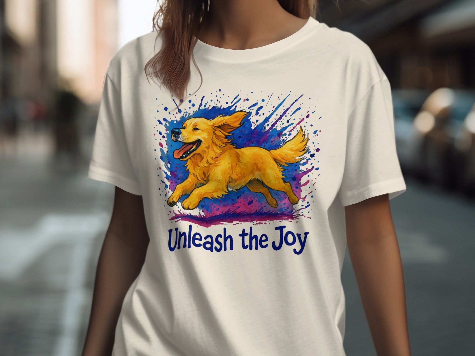 White t-shirt with a golden retriever running through colorful paint splatters, text "Unleash the Joy".
