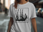Black dog on its back with legs in the air on a white t-shirt.