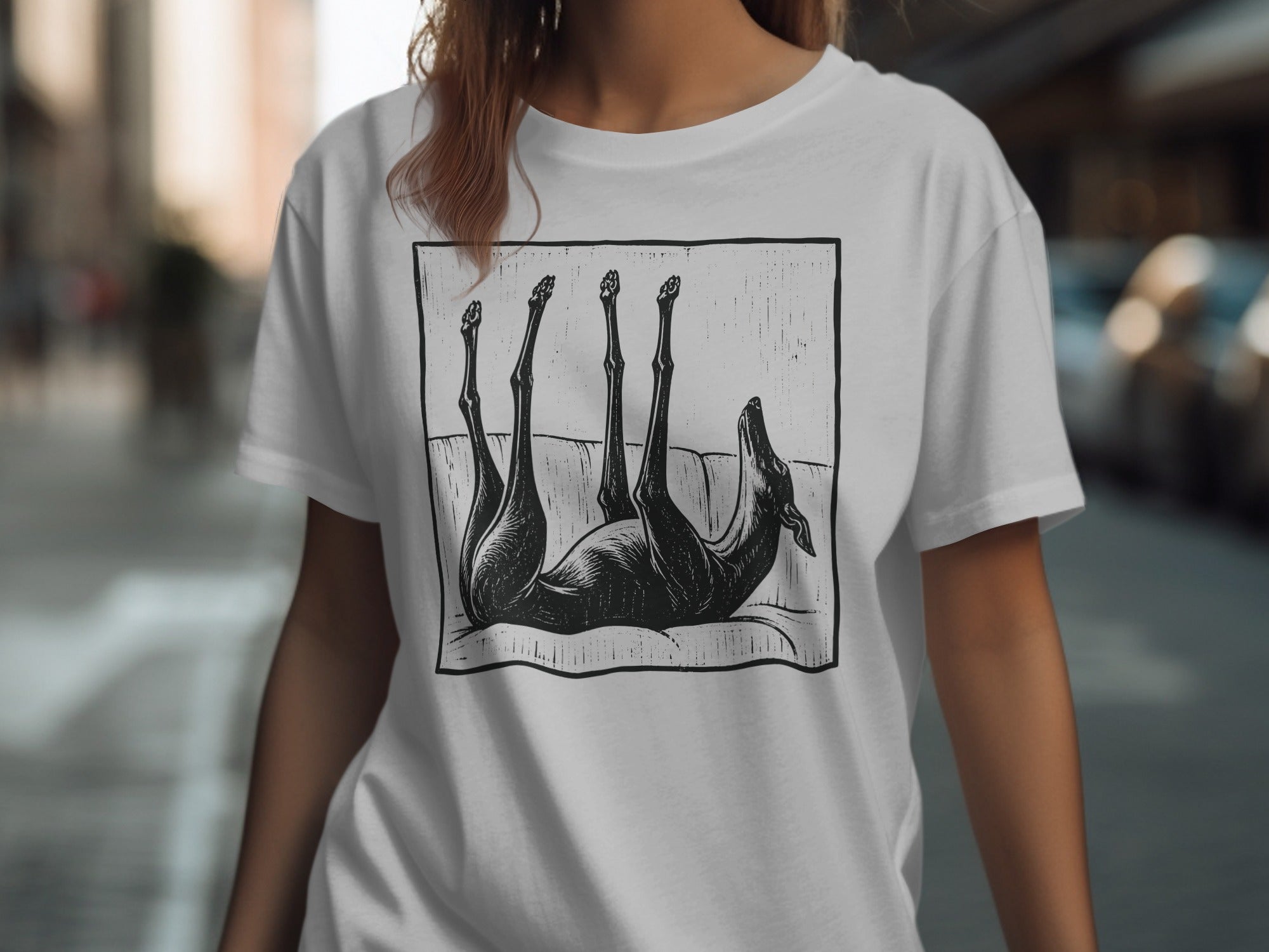 Black dog on its back with legs in the air on a white t-shirt.