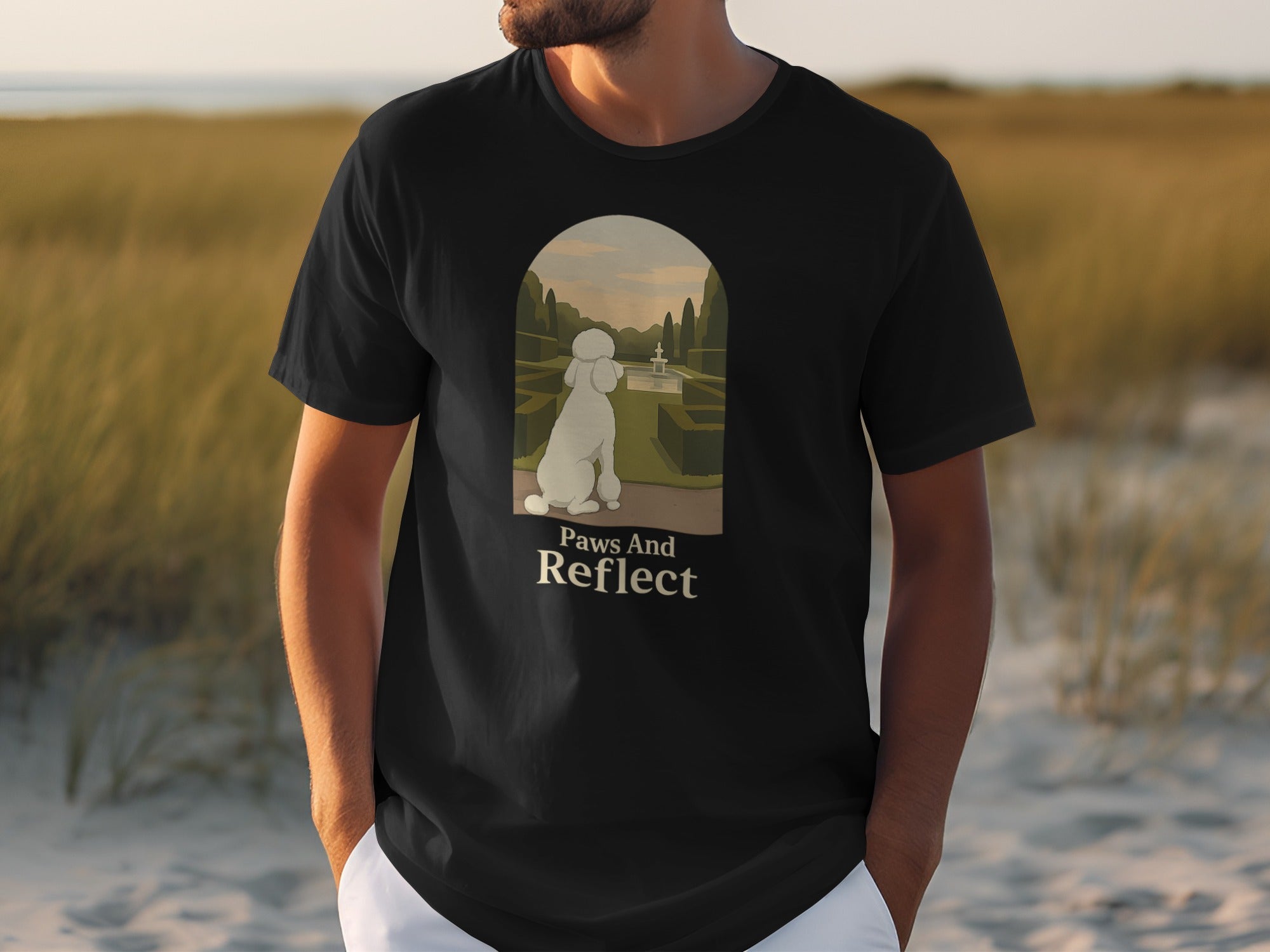 Black t-shirt with a white poodle in a garden and text "Paws And Reflect".