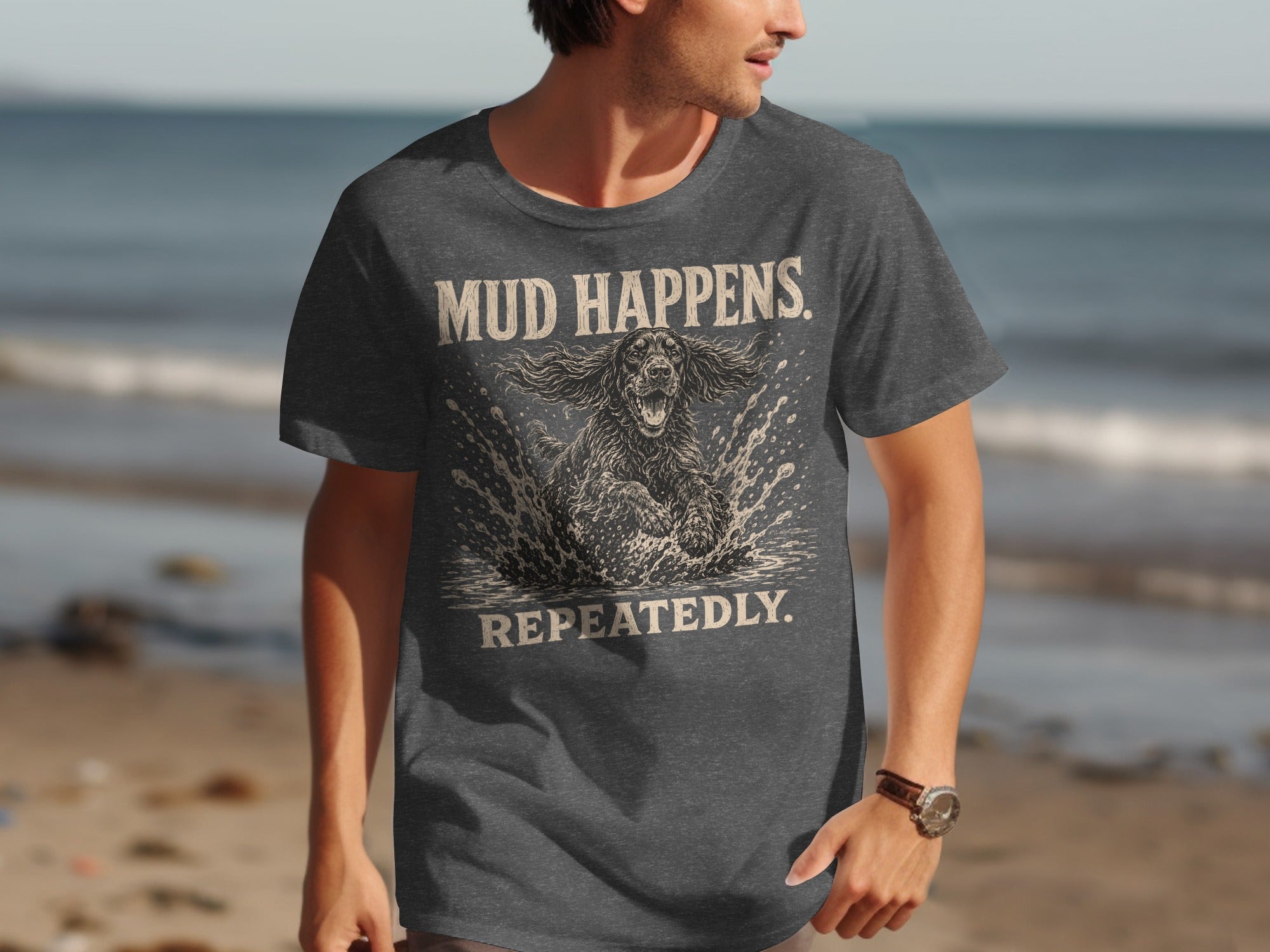Dark grey t-shirt with text "MUD HAPPENS. REPEATEDLY." and a dog splashing in mud.