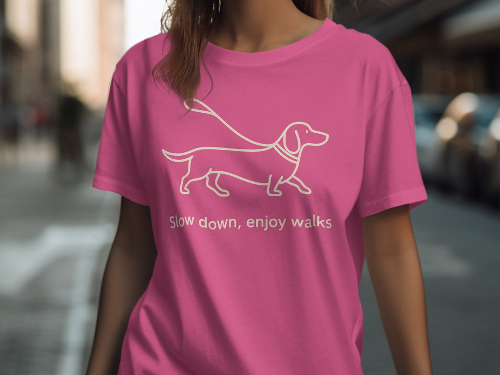 Pink t-shirt with white outline of a dachshund on a leash and text.