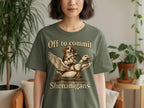 Green t-shirt graphic with dog riding a goose, text reads "Off to commit Shenanigans".