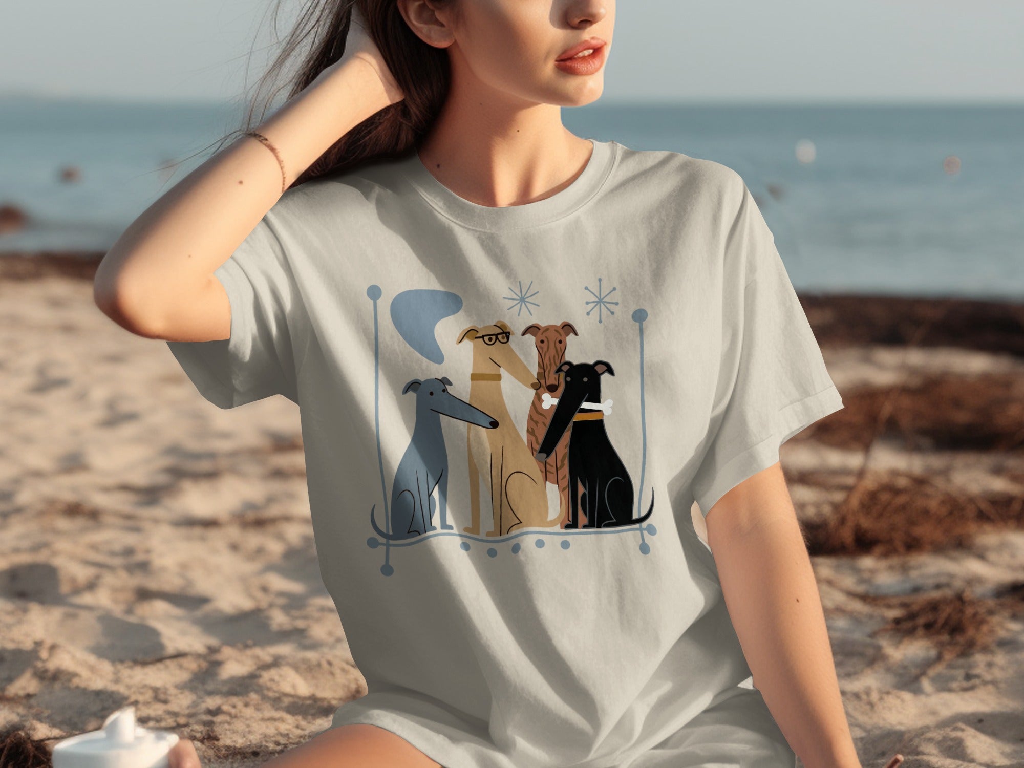Light gray t-shirt with cartoon greyhounds sitting on beach.