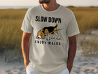 Man wearing a light gray t-shirt with "SLOW DOWN ENJOY WALKS" text and dog graphic.