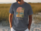T-shirt with arched graphic of dog on beach at sunset, text "Paws And Reflect".