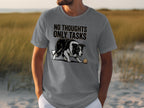 Man wearing a grey t-shirt with "NO THOUGHTS ONLY TASKS" and a dog with a ball.