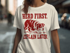 White t-shirt with dog graphic and text "HERD FIRST. EXPLAIN LATER."