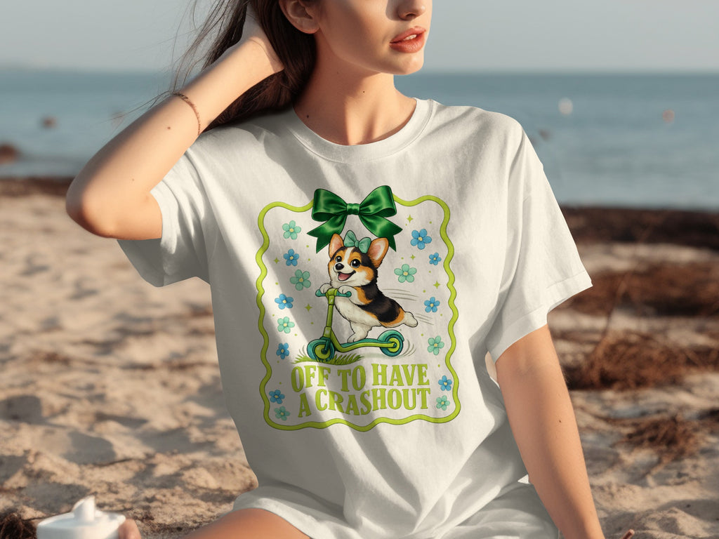 White t-shirt with a corgi riding a scooter and text "OFF TO HAVE A CRASHOUT".
