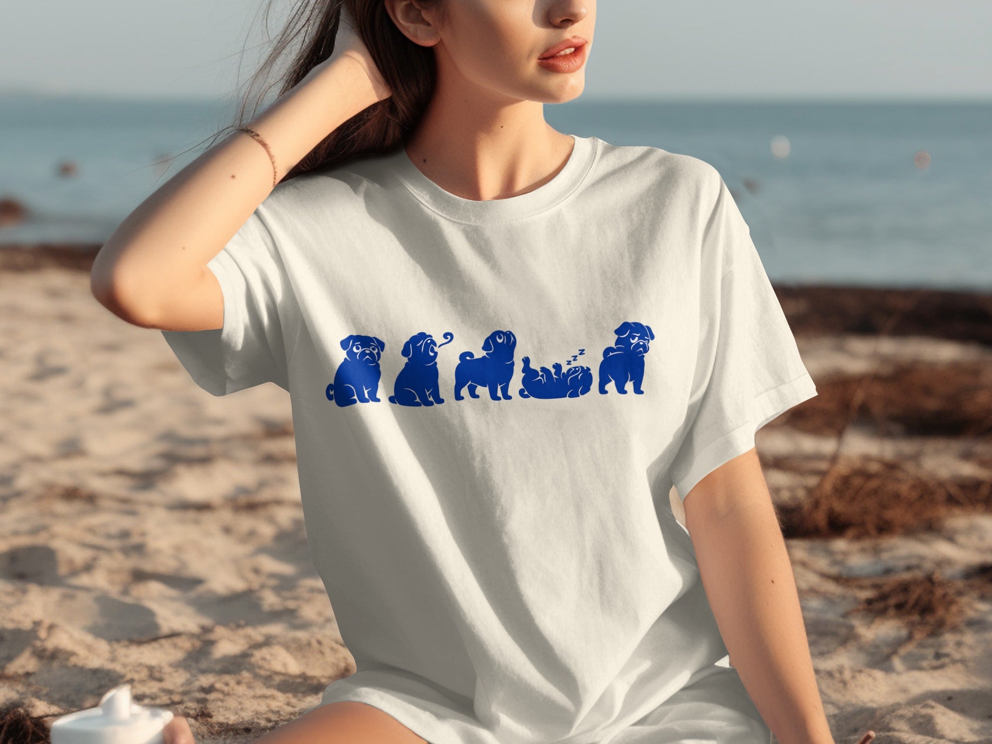White t-shirt with a blue graphic of pugs in various poses on a beach.