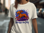 White t-shirt with a brown dog graphic and "Unleash the Joy" text.