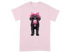 Black dog wearing sunglasses, pink bow, and bubblegum on pink t-shirt.