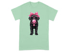Black Labrador puppy wearing sunglasses, a pink bow, and a pink collar with a heart tag.