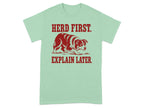 Mint green t-shirt with red text "HERD FIRST. EXPLAIN LATER." and dog illustration.